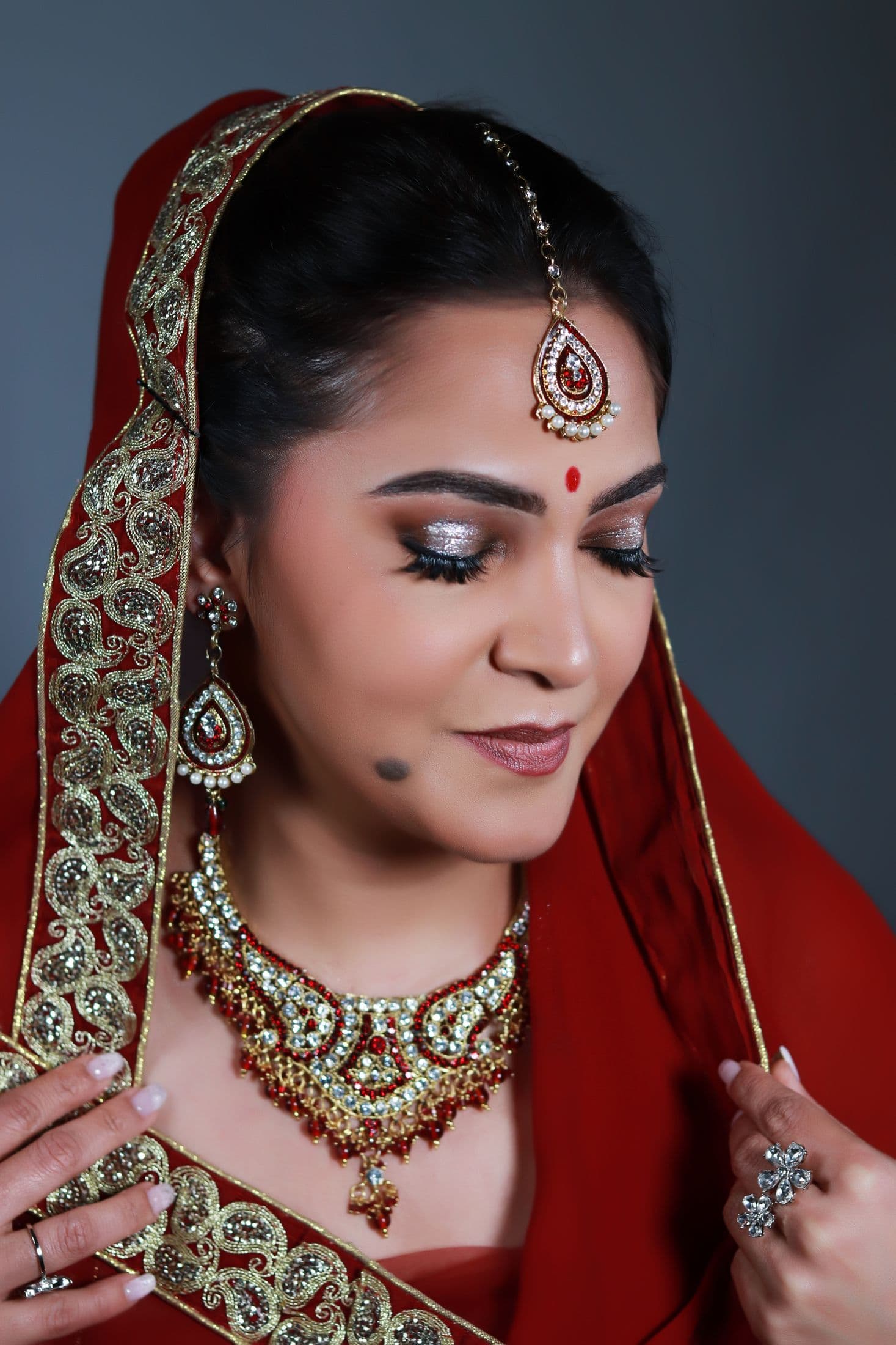 Bride in a red embroidered veil with silver shimmer eyes and red stone jewellery